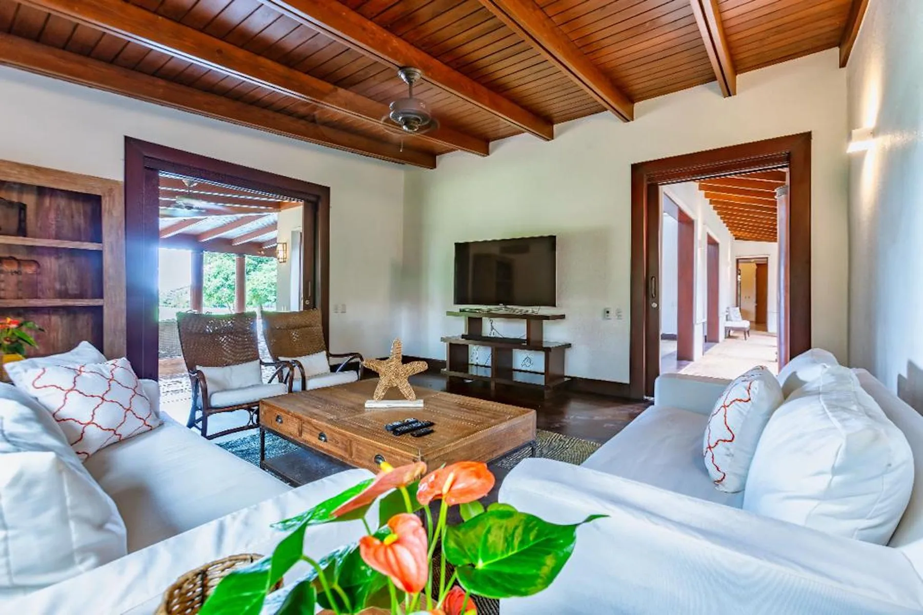 Una sala de estar con asientos blancos, una mesa de centro de madera y un televisor.
