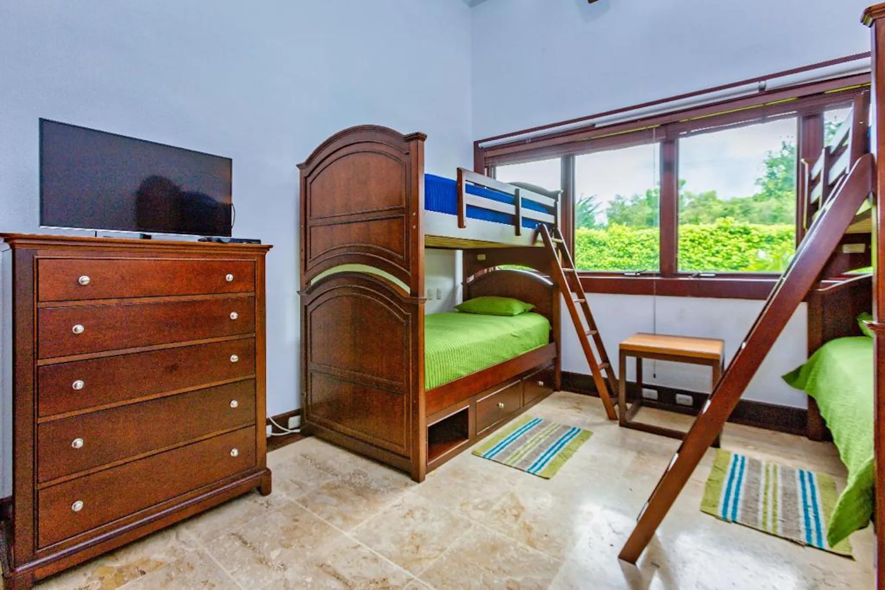Un dormitorio con literas de madera, una cómoda y una ventana grande.