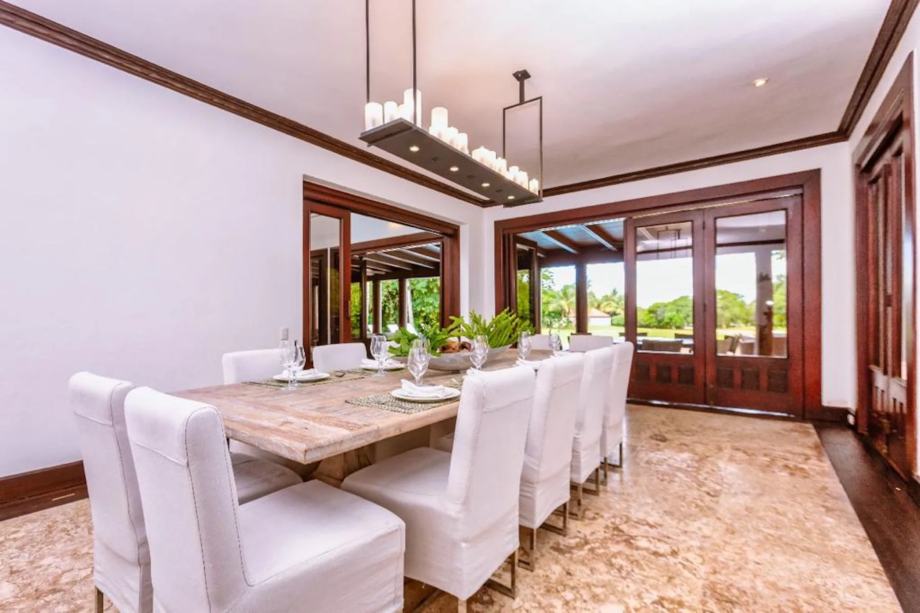 Un comedor con una mesa larga y asientos tapizados en blanco junto a grandes ventanas.