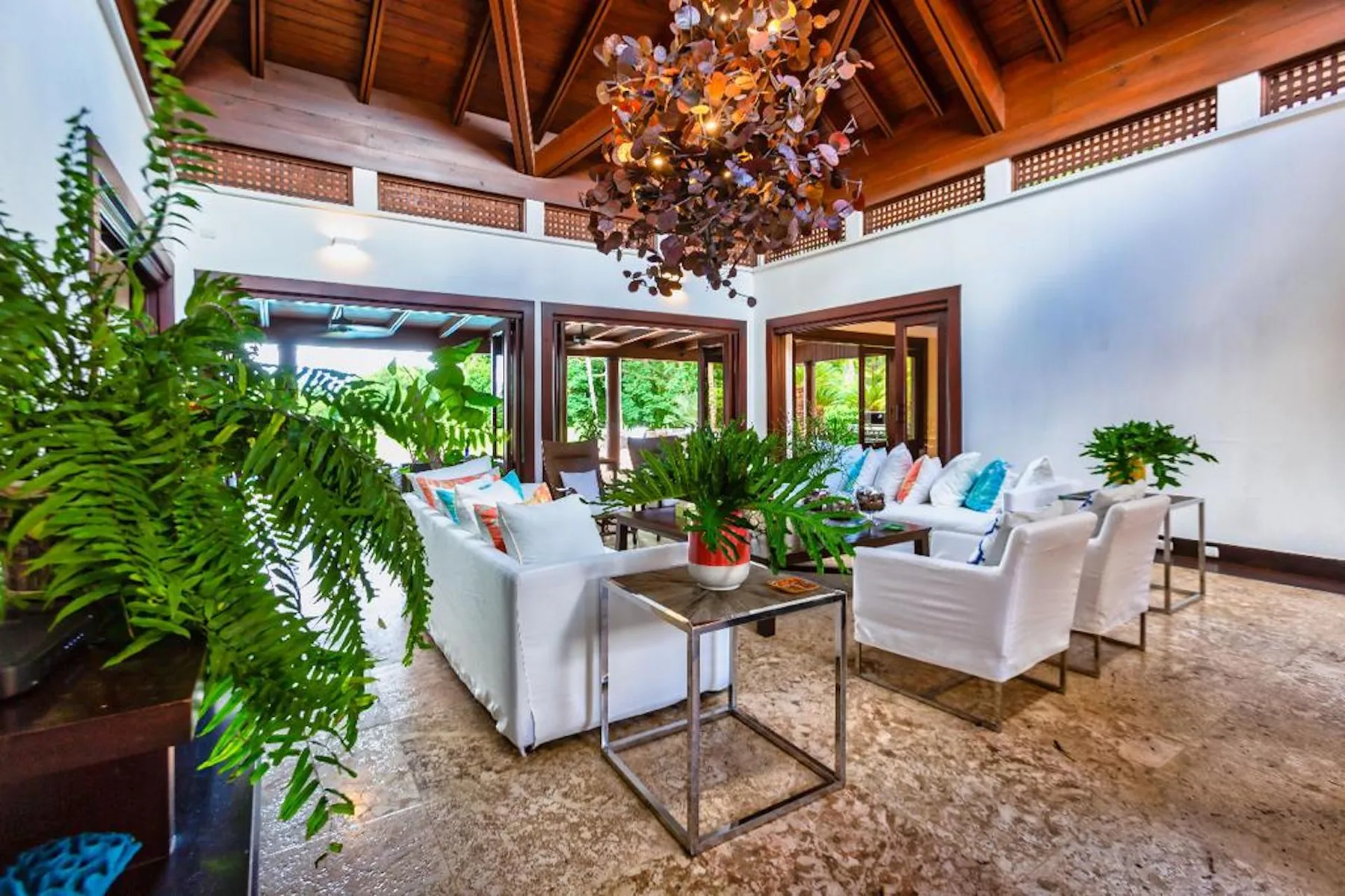 Una sala luminosa con asientos blancos, plantas frondosas y un techo alto de madera.