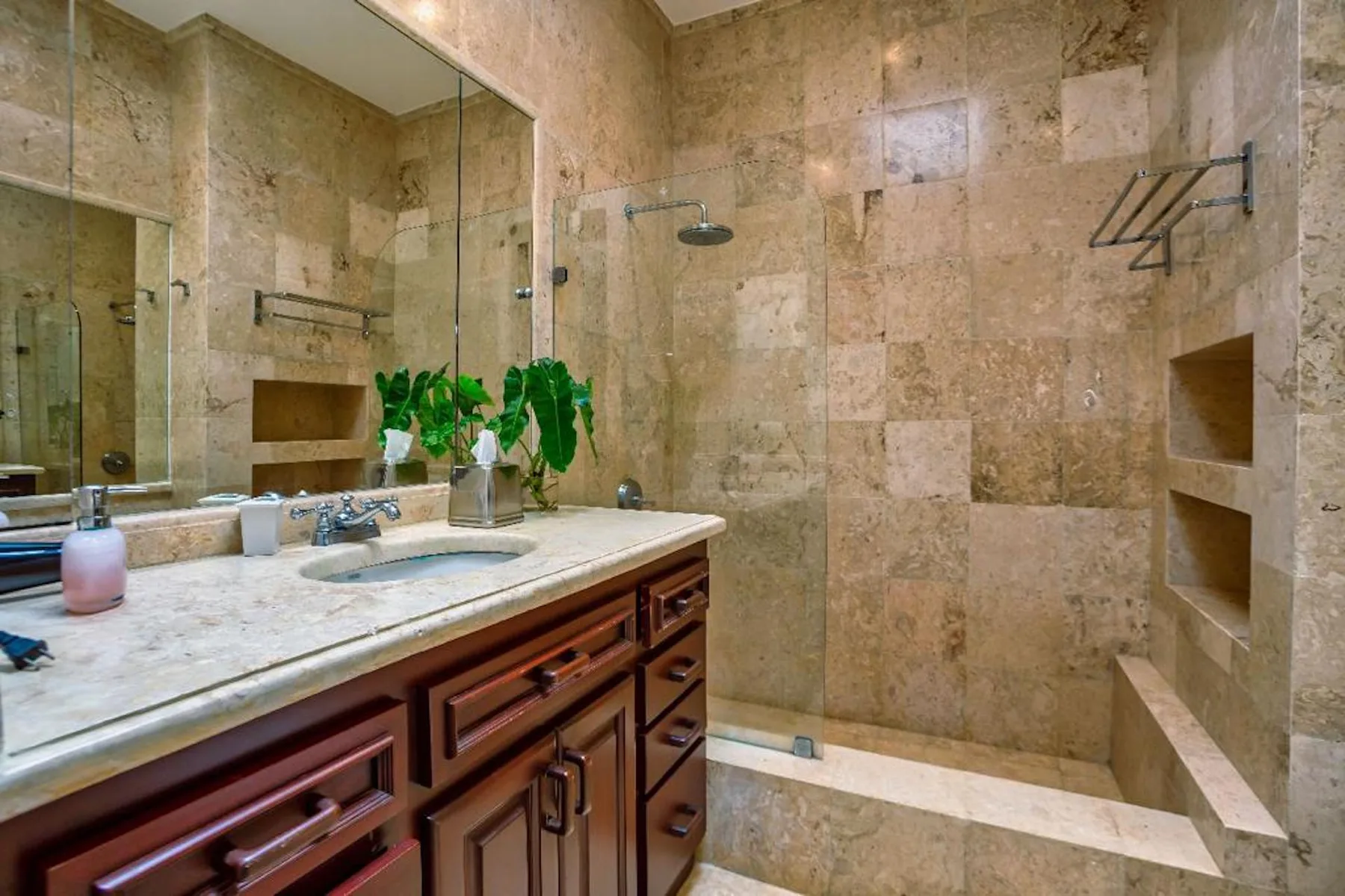 Un baño con azulejos de piedra, lavabo y ducha de vidrio.