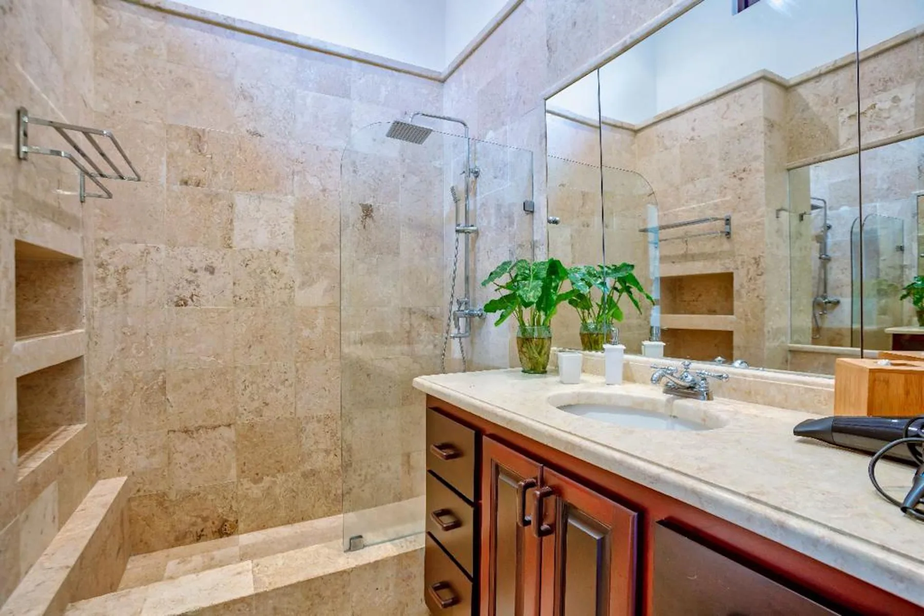 Un baño luminoso con ducha de vidrio, lavabo y un espejo grande.