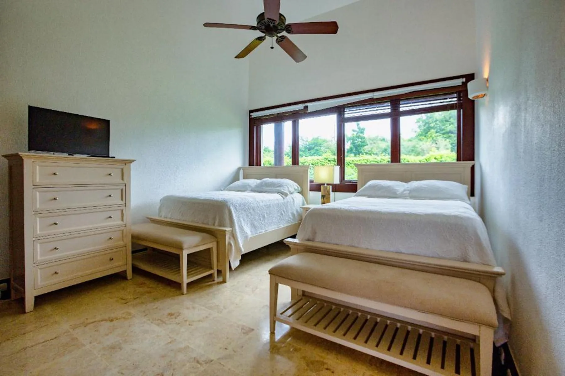 Un dormitorio con dos camas, una cómoda y una ventana grande con vista a la vegetación.