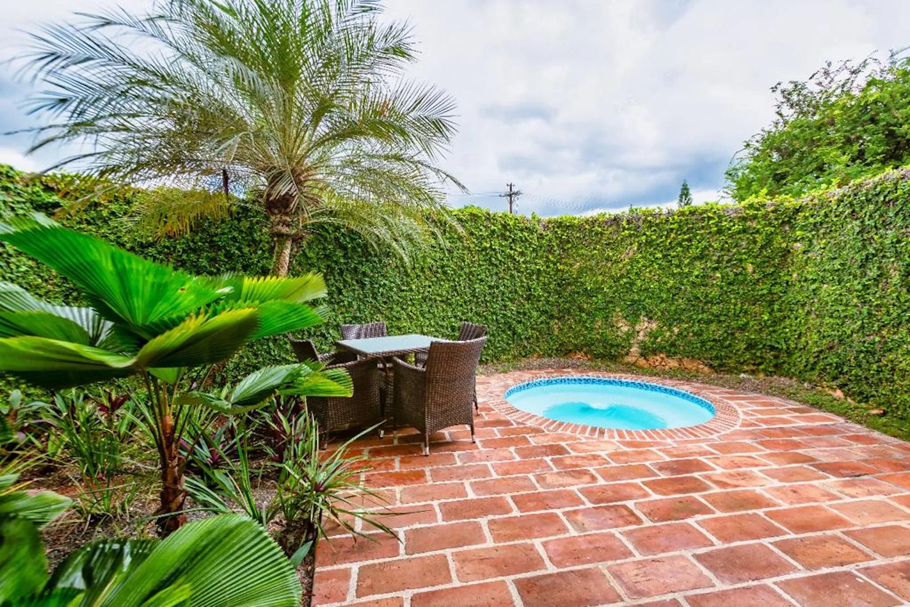 Un patio al aire libre con una pequeña piscina redonda y una mesa rodeada de vegetación.