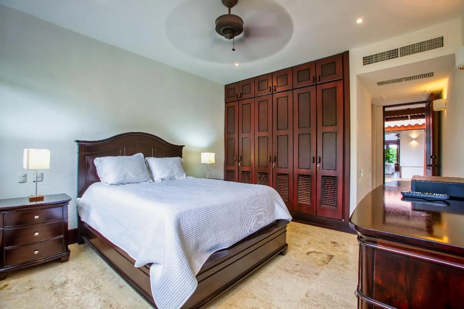 Un dormitorio con una cama grande, armarios de madera oscura y un ventilador de techo.