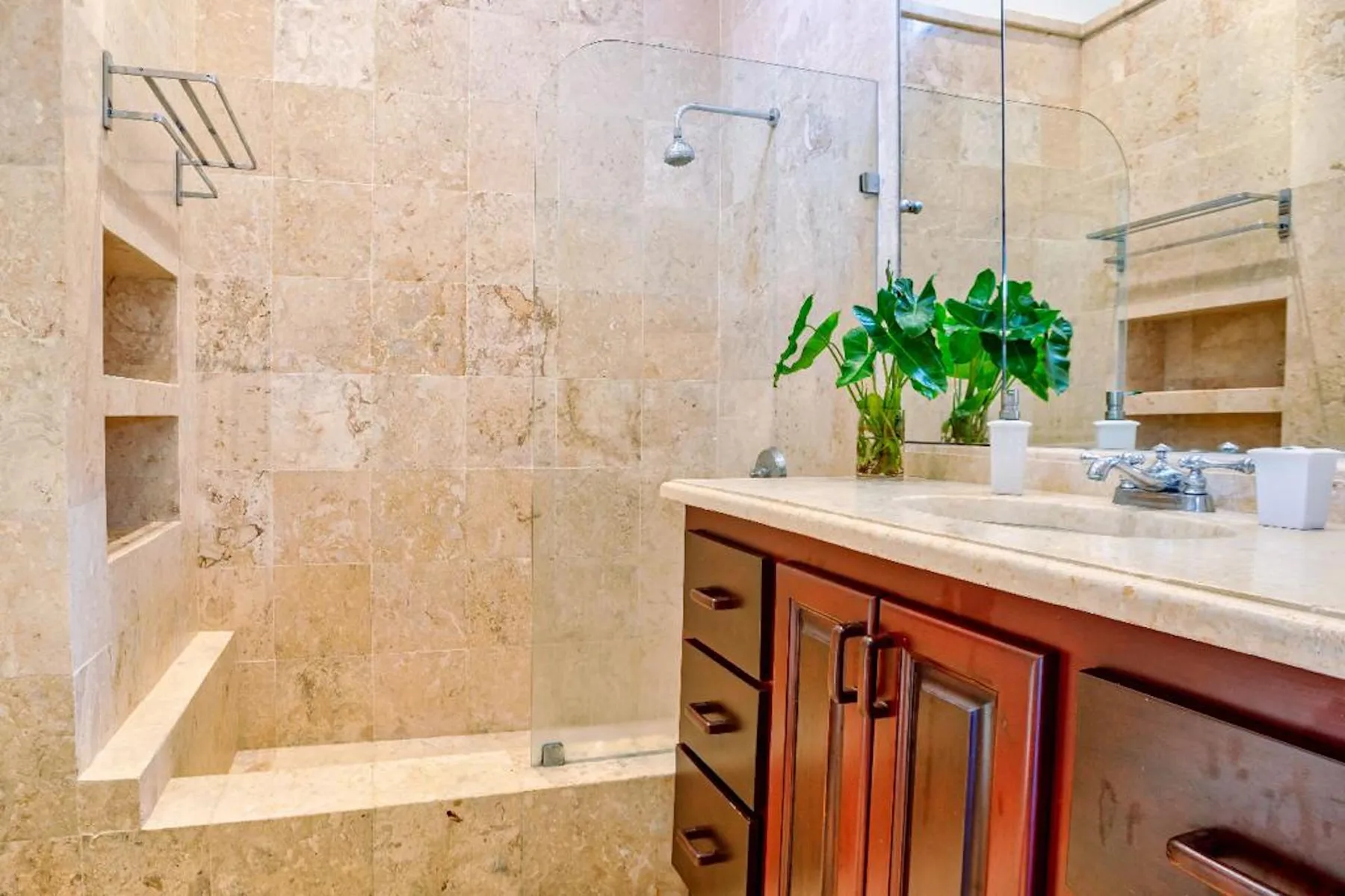 Un baño de piedra beige con ducha de vidrio y tocador de madera.