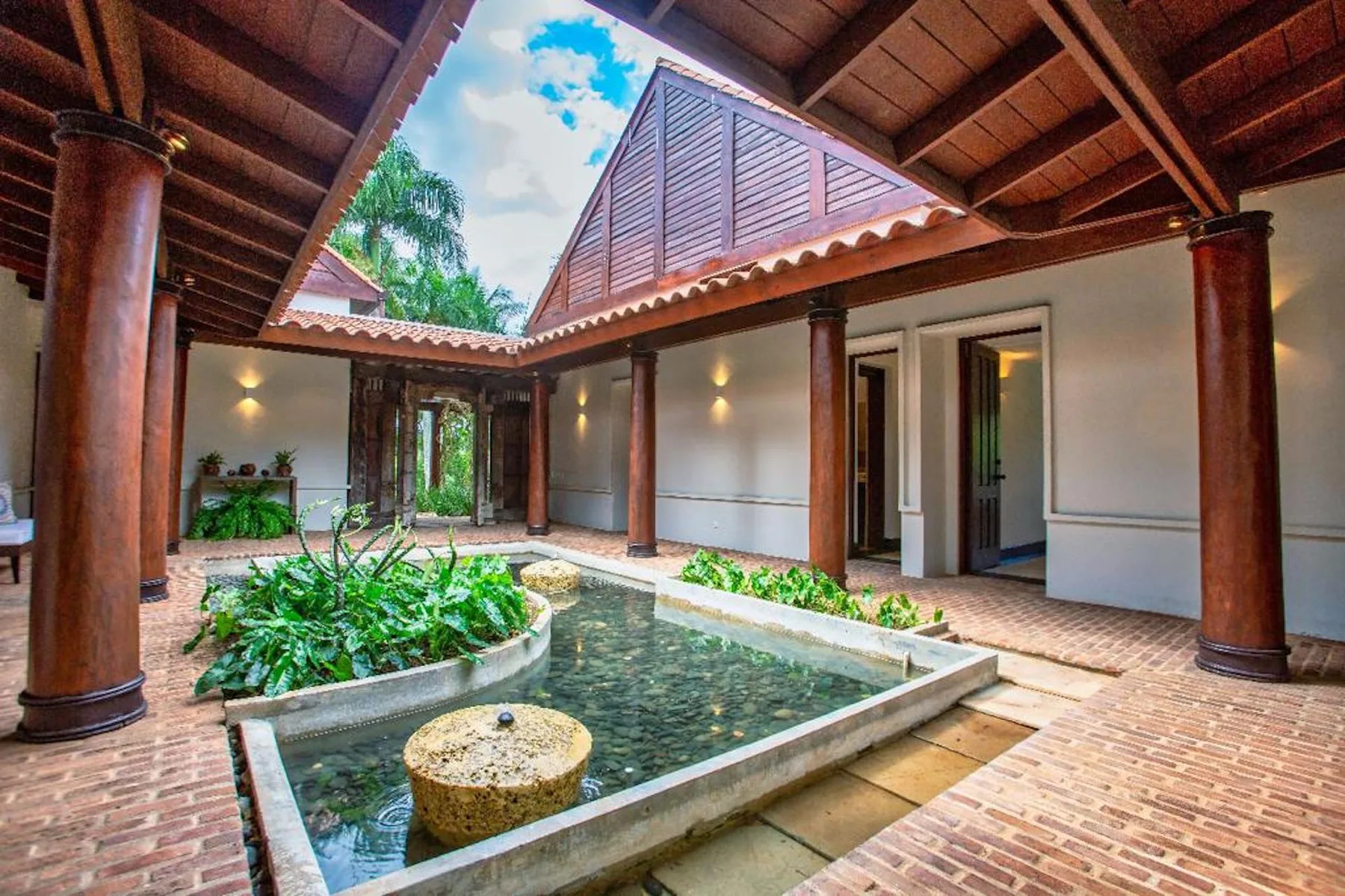 Un patio abierto al cielo rodea un estanque poco profundo y un jardín con plantas.