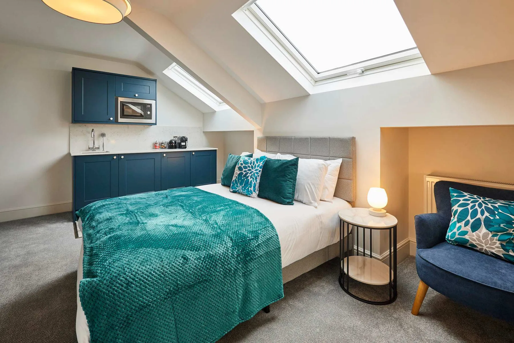 A bedroom with a bed dressed in teal bedding beneath a skylight.
