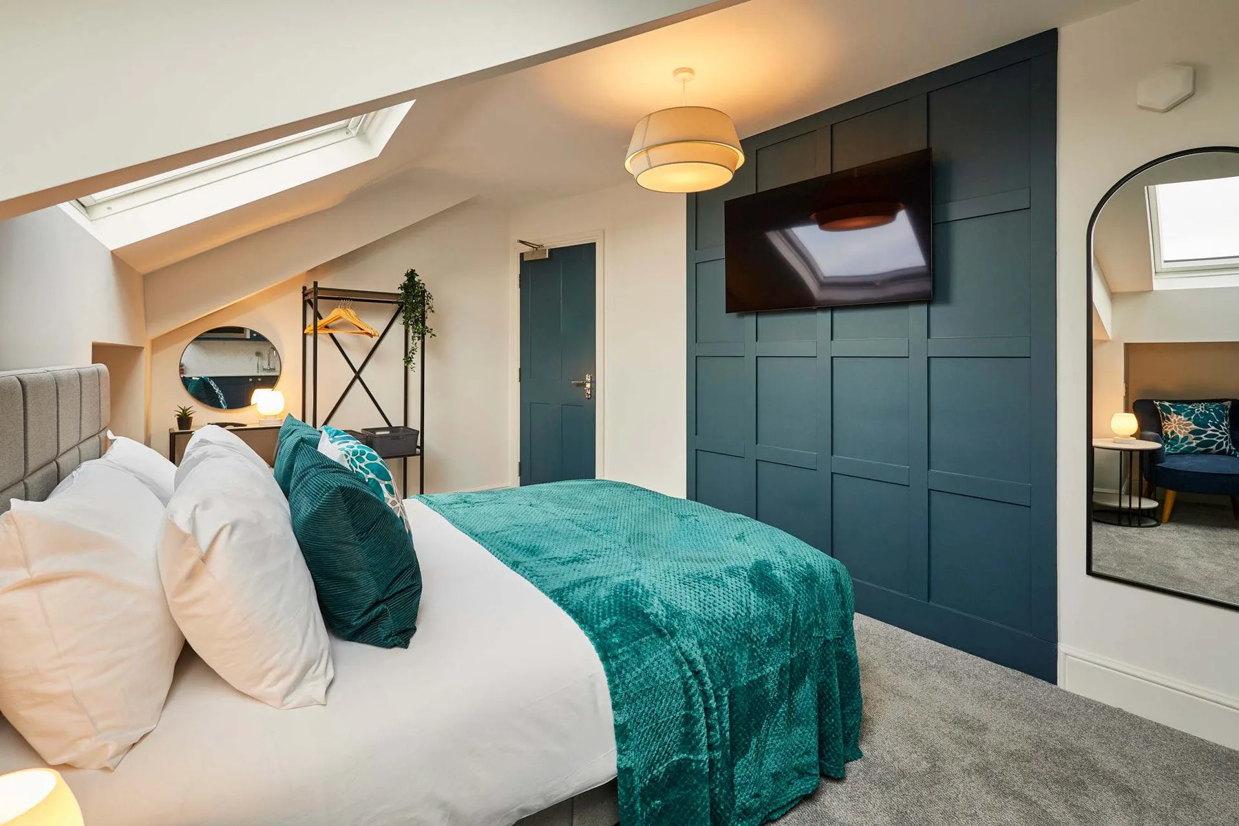 A bedroom with a bed dressed in white and teal bedding beneath a skylight.