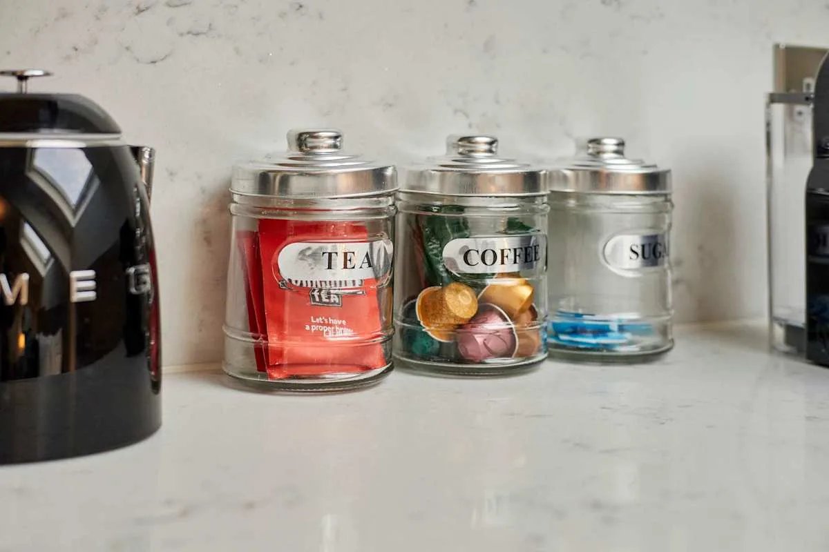 Tea, coffee, and sugar containers sit on a kitchen counter beside a kettle.