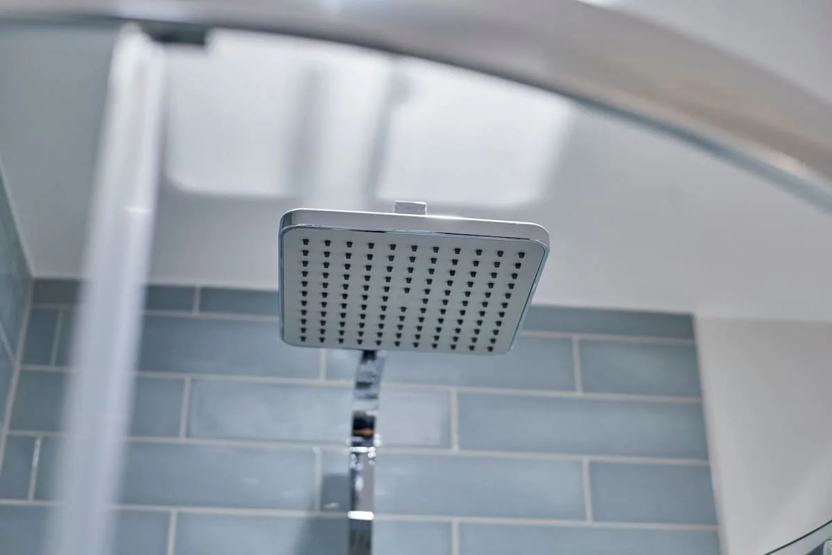 A showerhead is mounted above blue-gray tiled walls.