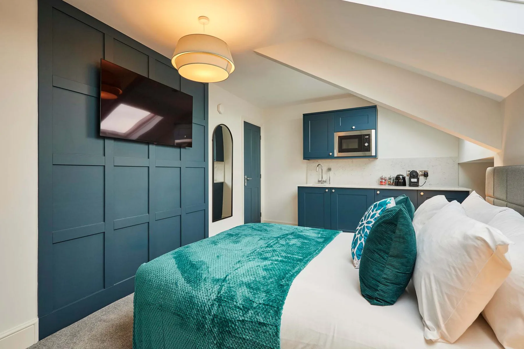 Un dormitorio con una cama, ropa de cama color turquesa y un televisor en la pared.