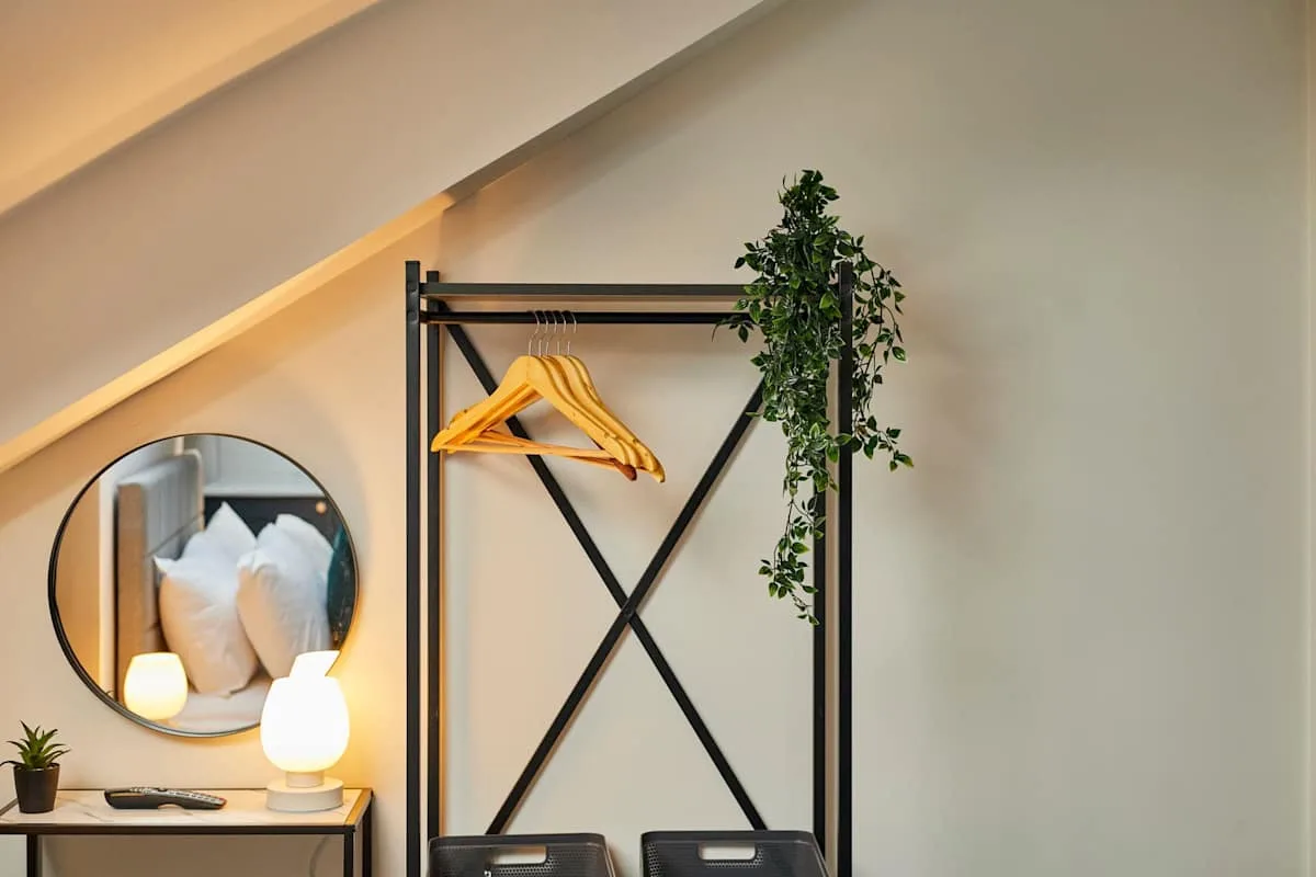 A bedroom dressing area with a clothes rack, hangers, and a round mirror.