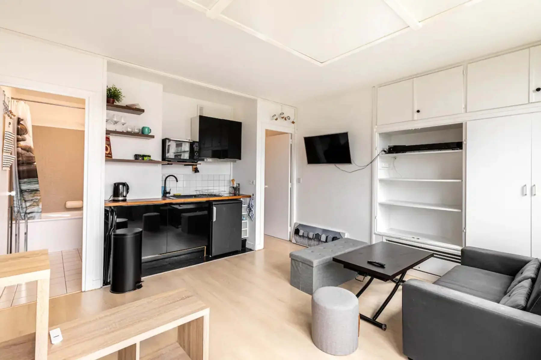 Una luminosa sala de estar tipo estudio con cocina pequeña, estantes y asientos.