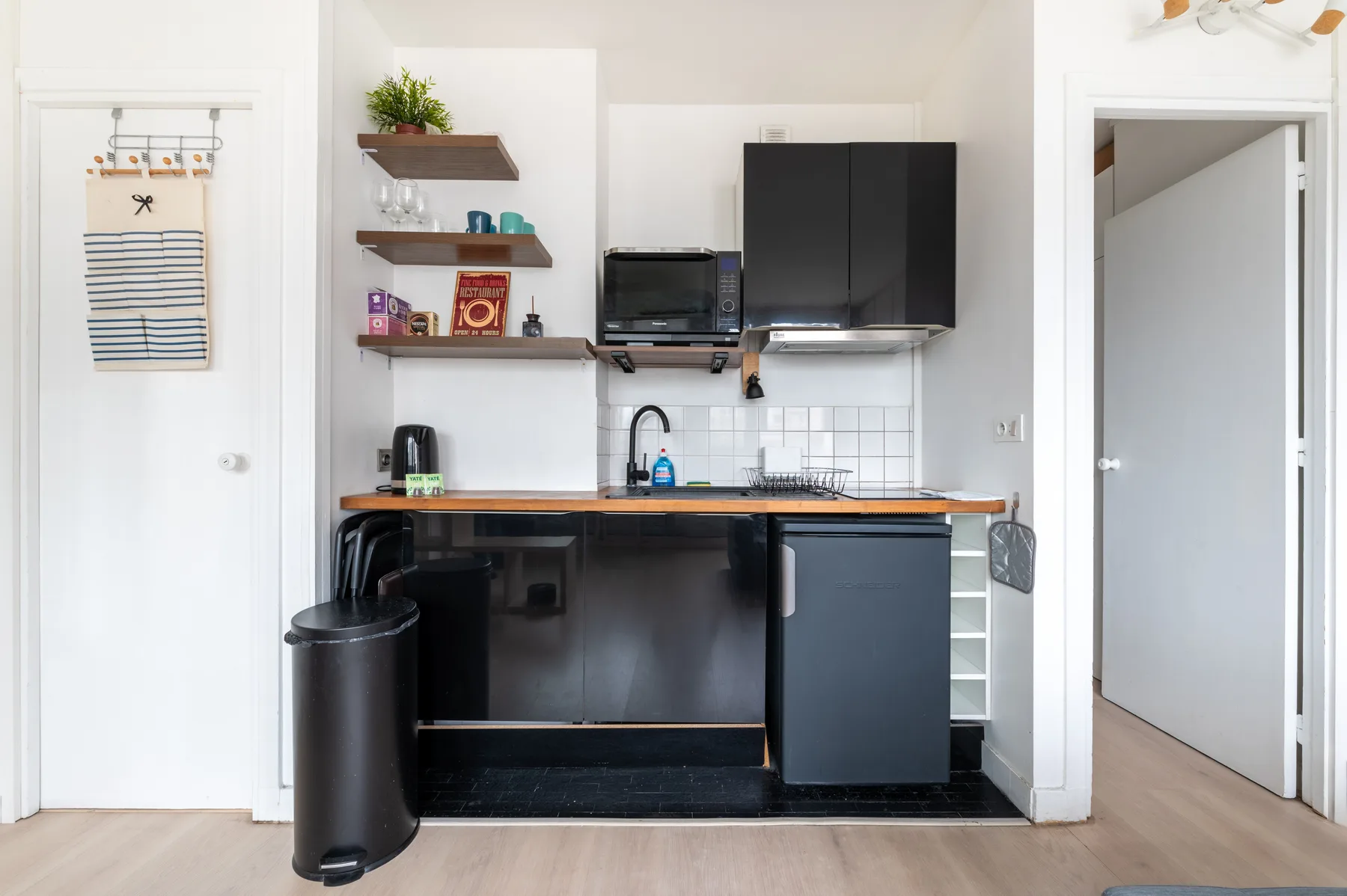 Una cocina compacta con gabinetes oscuros, fregadero y estantes abiertos.