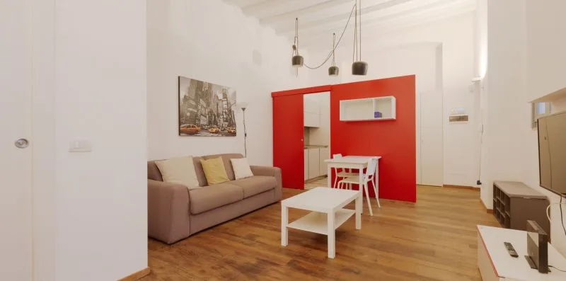 A bright living room with seating, a coffee table, and a red accent wall.