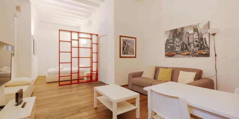 A bright living room with a sofa, dining table, and red-framed divider.
