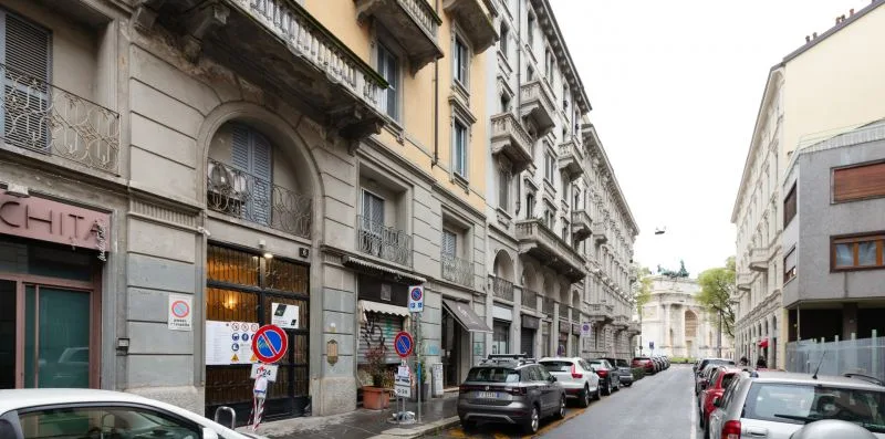 An urban street lined with multi-story buildings and parked cars.