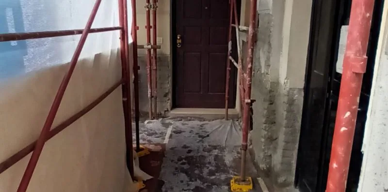 A narrow construction passage leads to a dark wooden door.