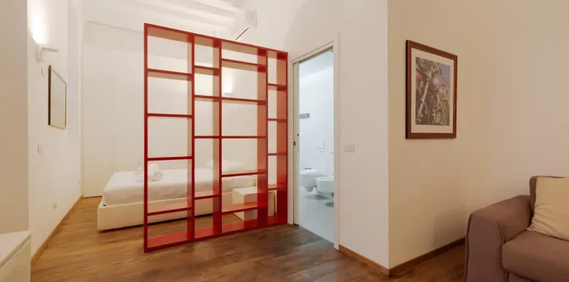 A bedroom with a bed behind a red open shelving divider.