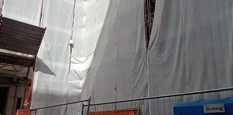 A construction area is covered with large white protective sheets beside metal scaffolding.