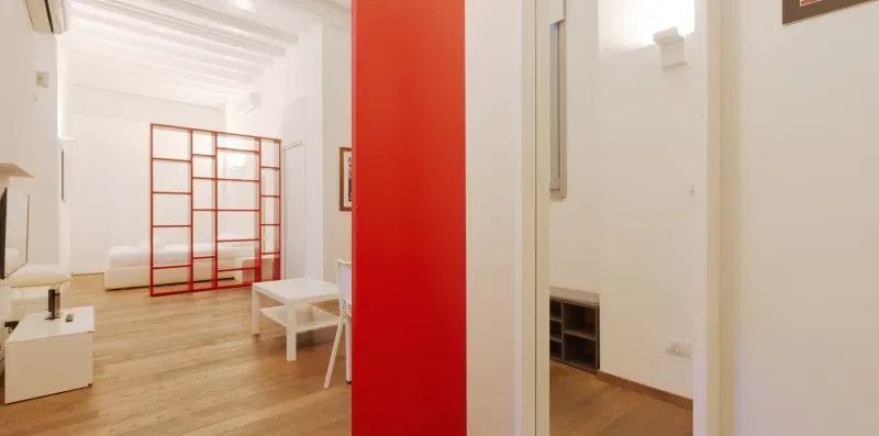 A bright interior hallway with a red partition and light wood flooring.