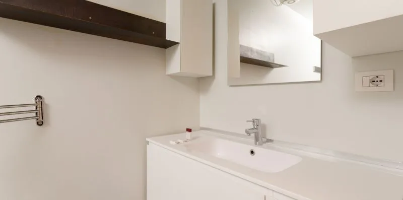 A bathroom vanity with a sink, mirror, and wall-mounted towel bar.