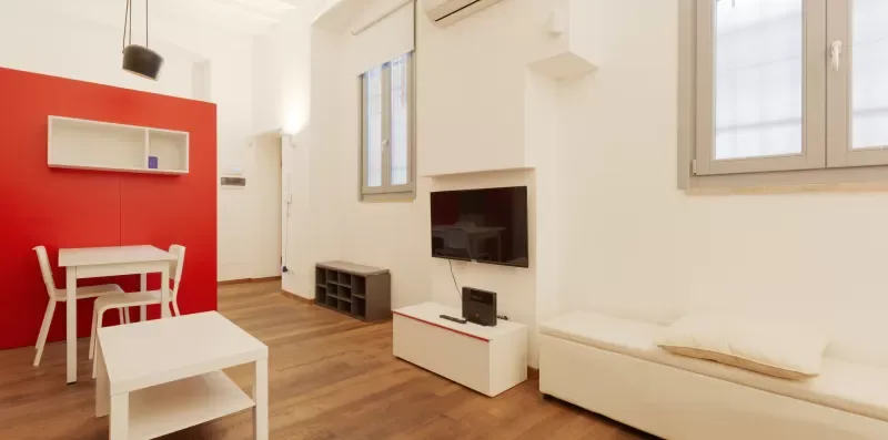 A bright living room with a television, dining table, and white seating.
