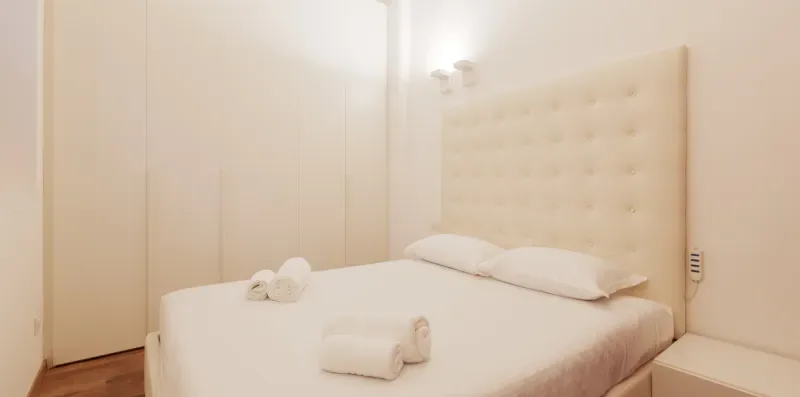 A bedroom with a neatly made bed and folded towels.