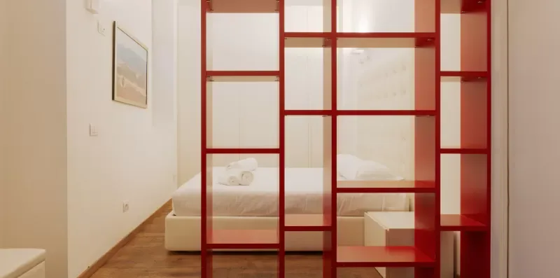 A bedroom with a bed behind a red open-frame room divider.