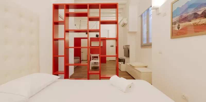 A bright bedroom with a white bed and a red open partition.