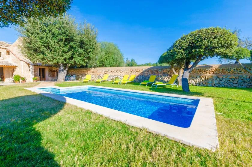 Una piscina al aire libre está en un jardín con césped, junto a muros de piedra y árboles.