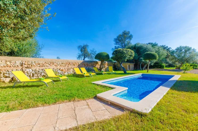 Una piscina al aire libre junto a un césped con tumbonas.