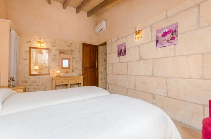 Un dormitorio con ropa de cama blanca, vigas expuestas y paredes claras de piedra.