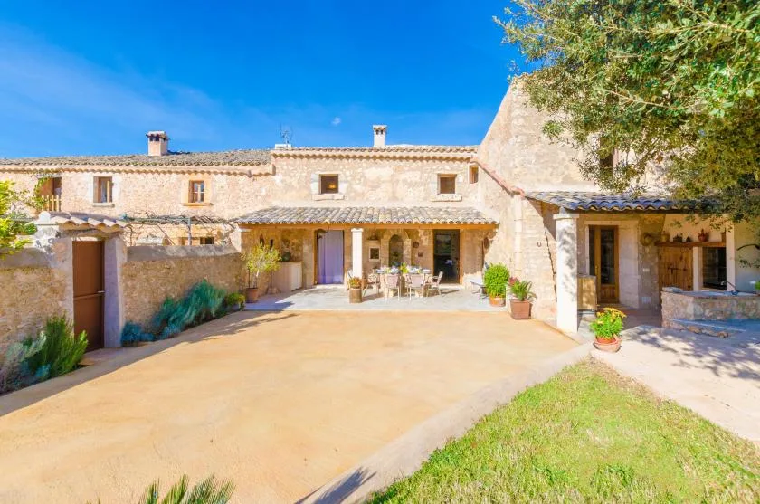 Una casa de piedra da a un patio soleado con asientos al aire libre.
