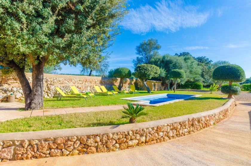 Una piscina exterior está en un jardín con un muro de piedra y tumbonas.
