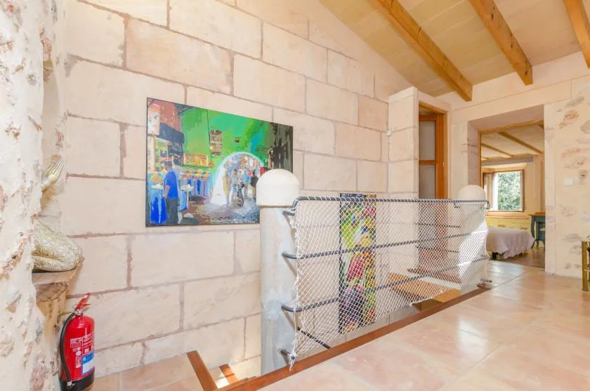 Un pasillo interior de paredes de piedra, con arte colorido y una barandilla metálica.
