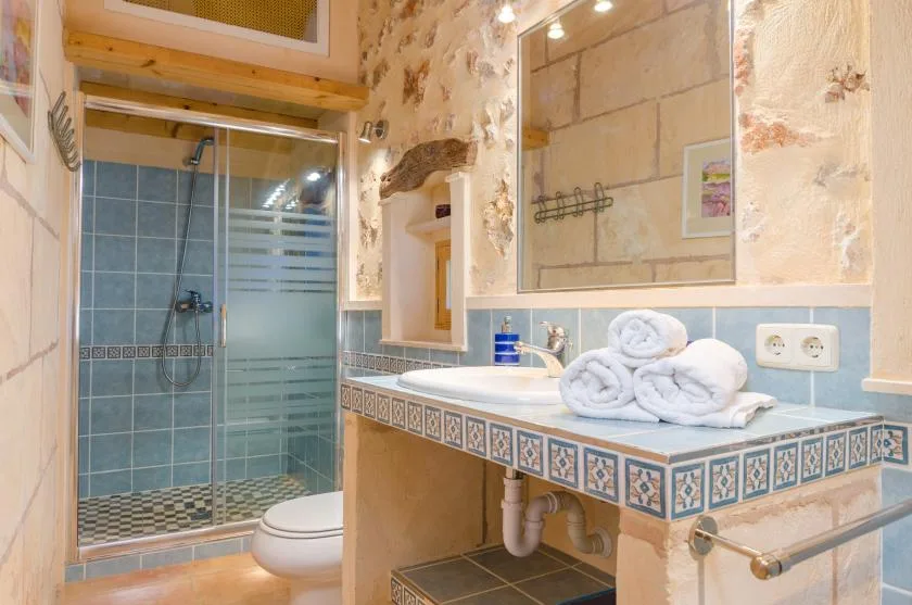 Un baño alicatado con ducha de vidrio, lavabo y toallas dobladas.