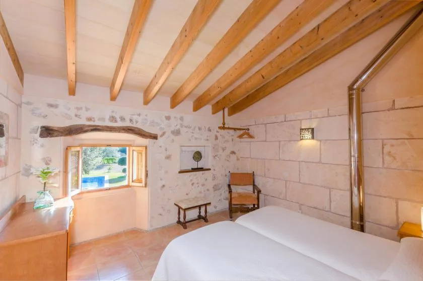Un dormitorio con una cama, vigas de madera en el techo y una ventana pequeña.