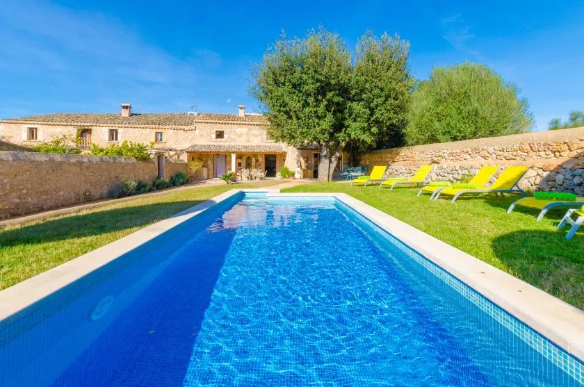 Una piscina al aire libre está junto a una casa de piedra y una zona de césped con asientos.