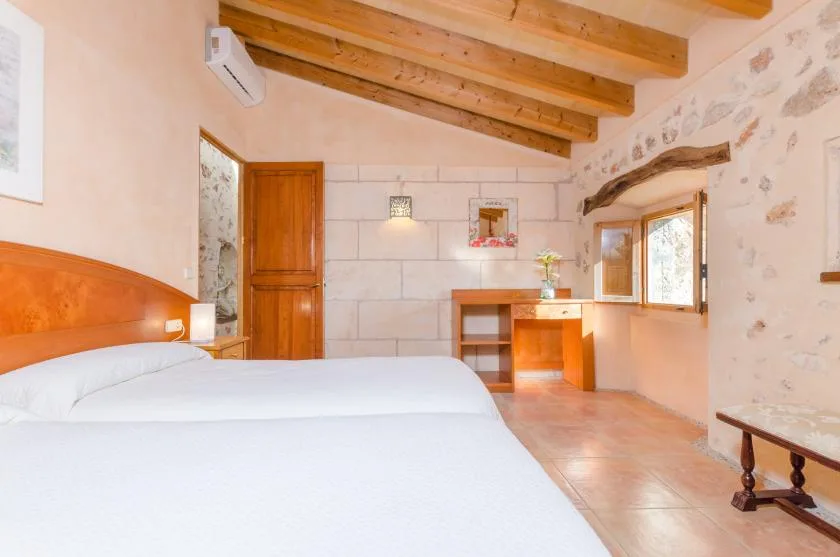 Un dormitorio con una cama, vigas de madera en el techo y un pequeño escritorio junto a la ventana.