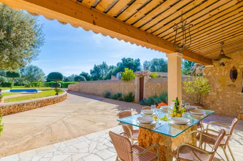 Una zona de comedor exterior cubierta da a un patio pavimentado y un jardín.