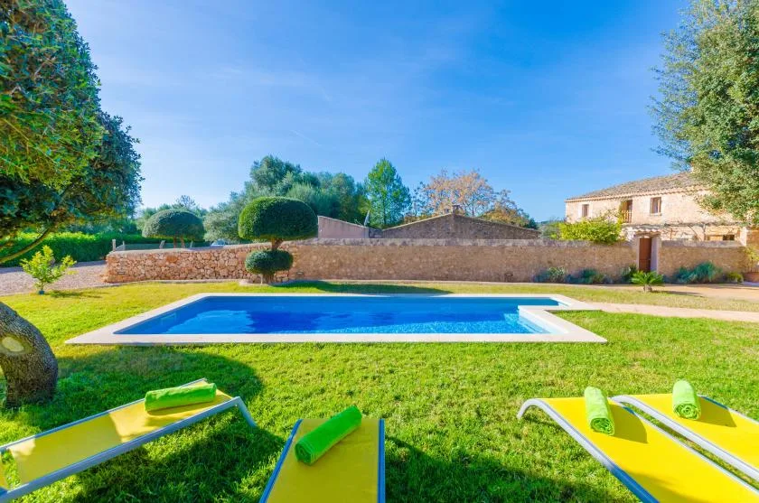 Una piscina está en un jardín con césped y tumbonas de colores vivos cerca.