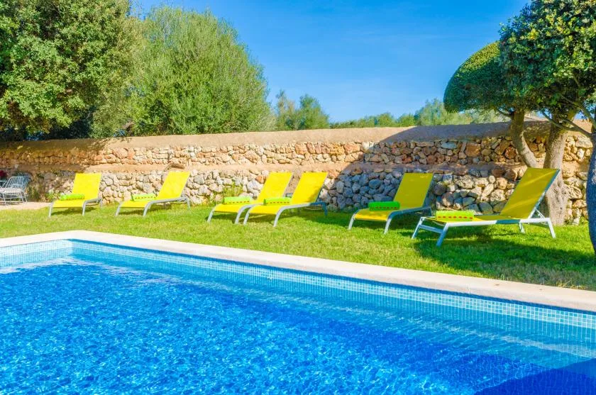 Una piscina al aire libre junto a césped y asientos de descanso.