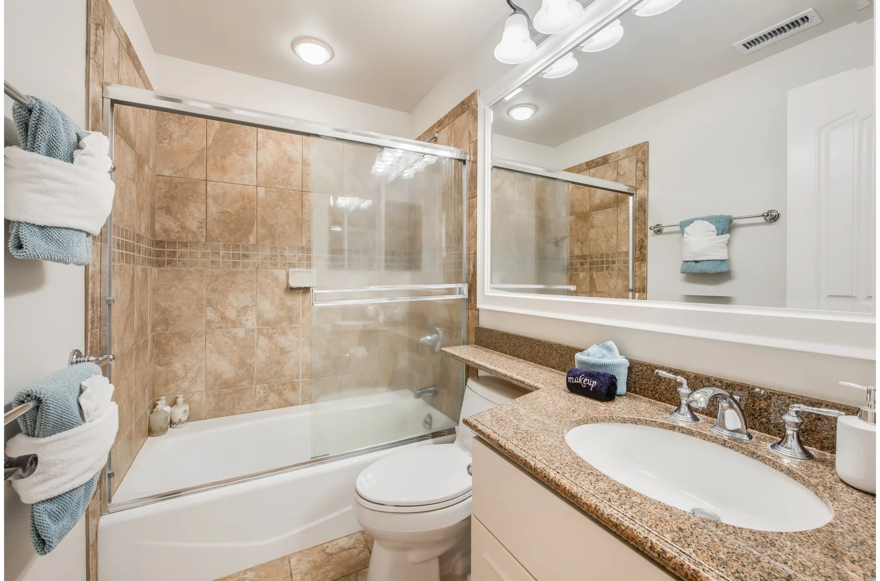 A bathroom with a bathtub and glass shower screen beside a sink and mirror.