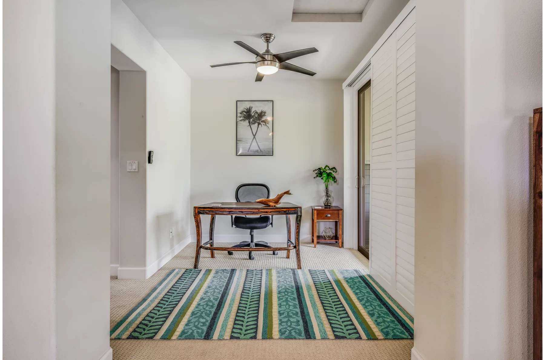 A bright workspace with a desk and chair beside a patterned rug.