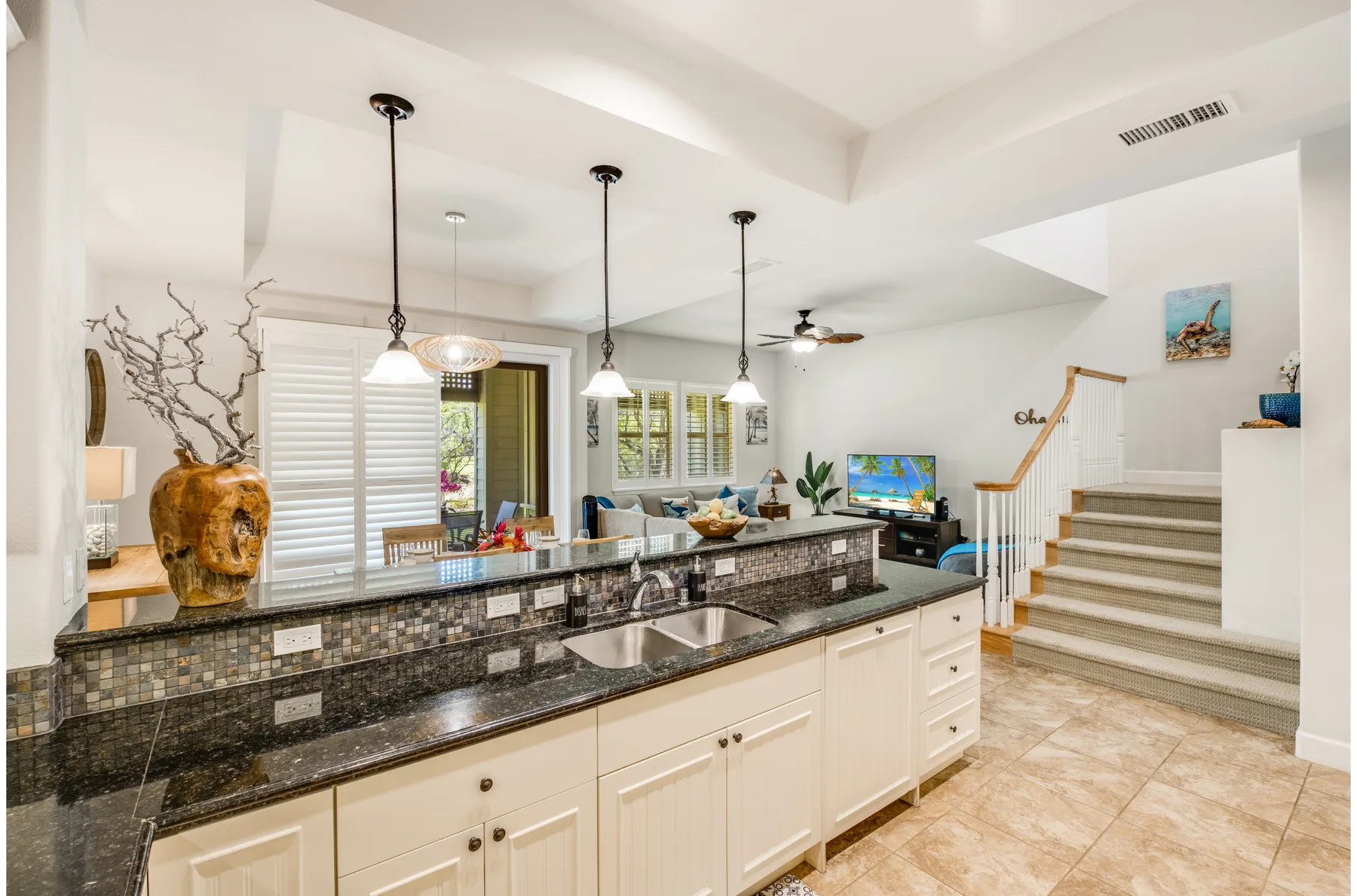 A bright kitchen with a long island, pendant lights, and stairs nearby.