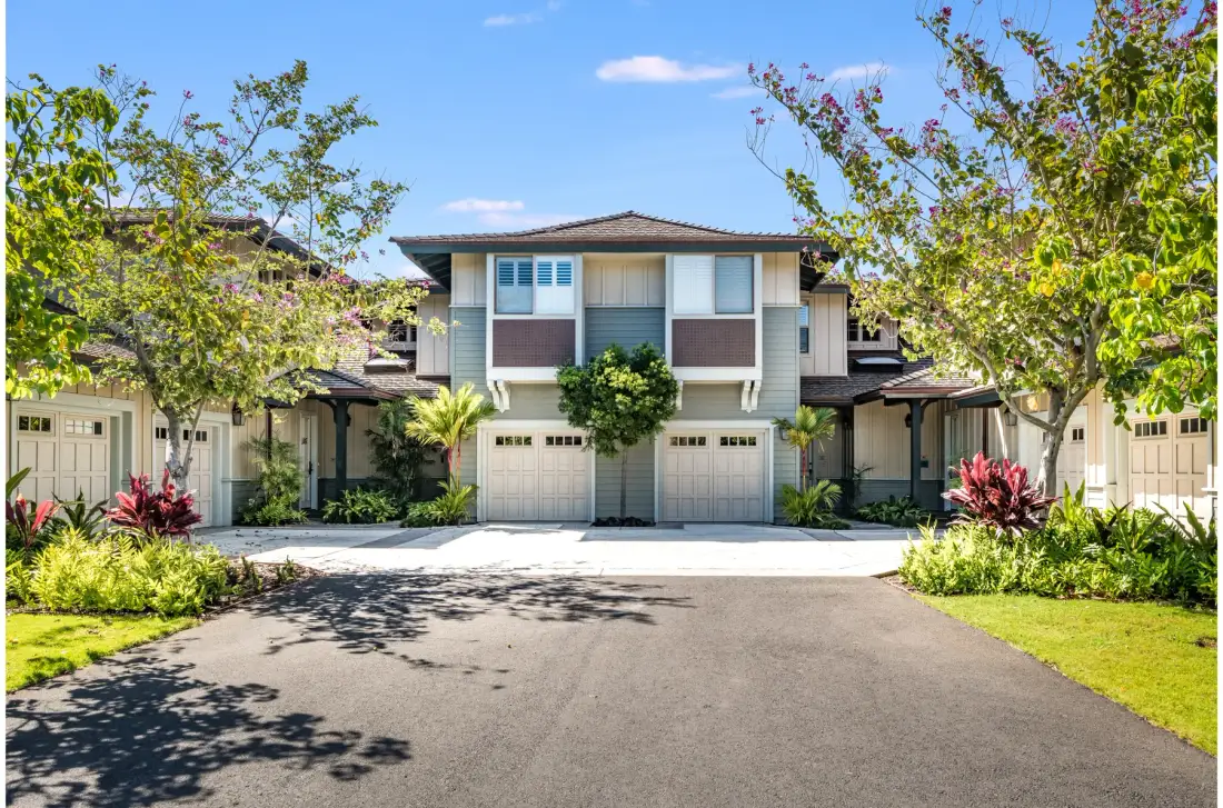 A residential building with a central upper floor, garage doors, and landscaped greenery.