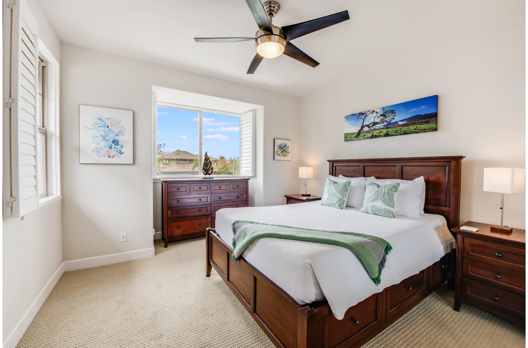 A bedroom with a wooden bed, green-accented white bedding, and a dresser beneath the window.