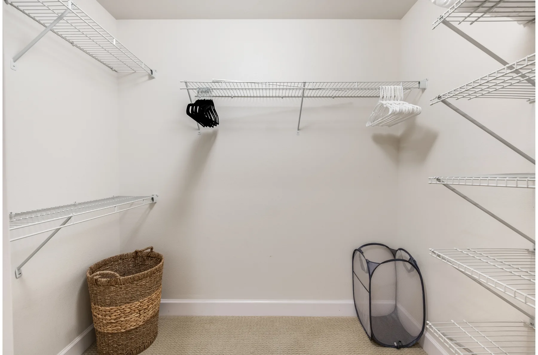 A walk-in closet with wire shelving, hangers, and a woven basket.